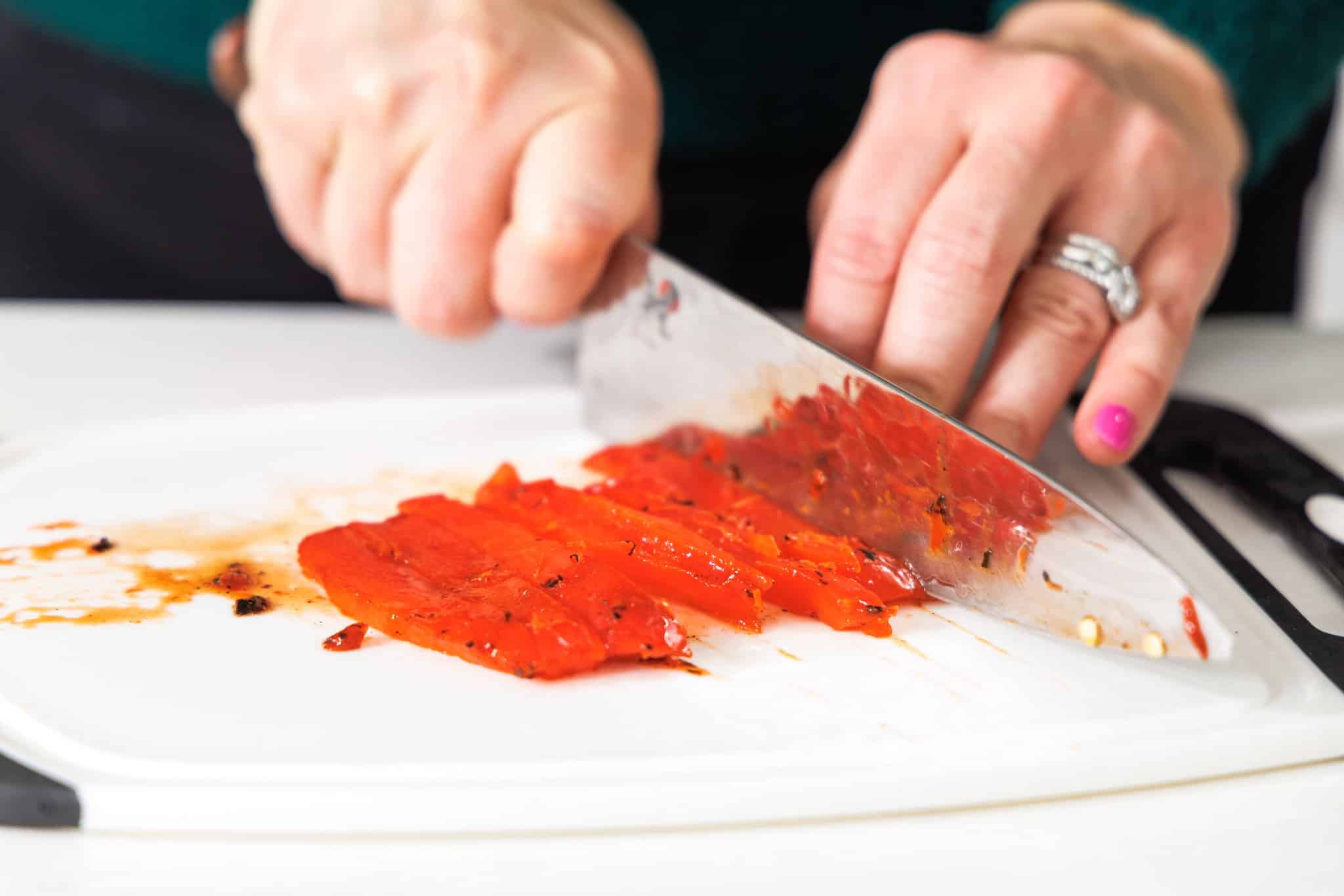 Using a sharp knife to slice roasted red bell pepper.